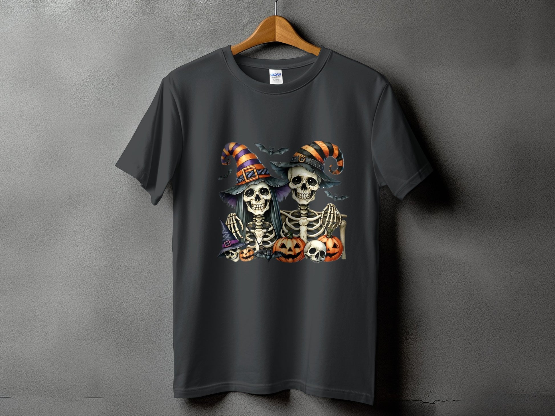 Two skeletons in witch hats with pumpkins and bats on a dark t-shirt.