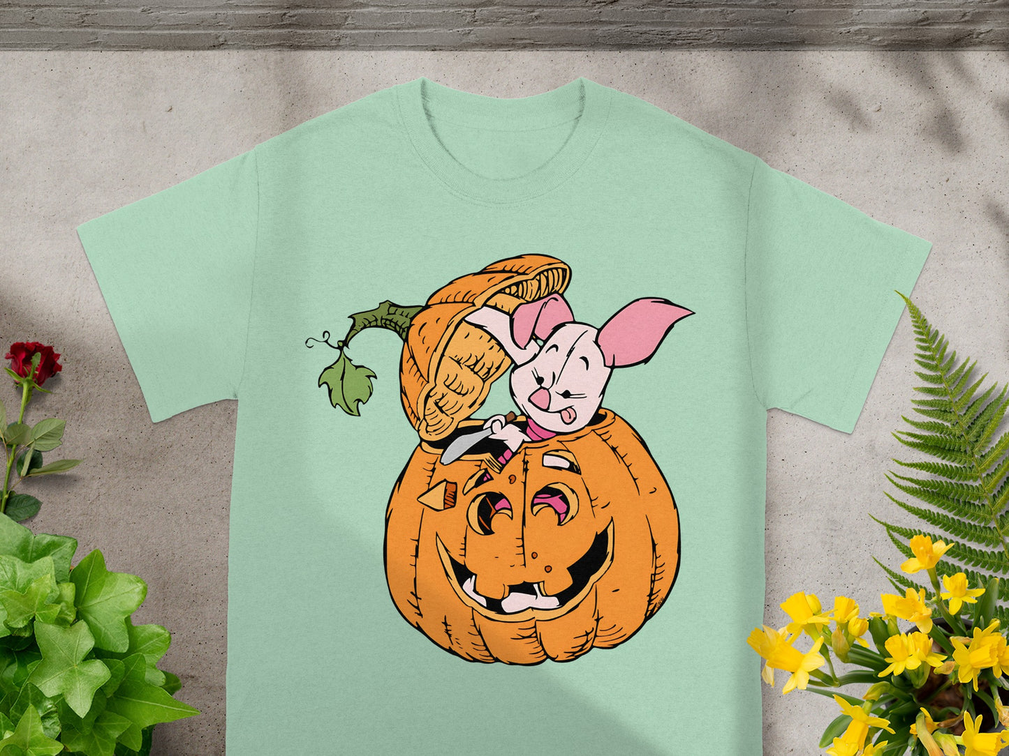 Piglet peeking out of a carved pumpkin on a light mint green t-shirt.
