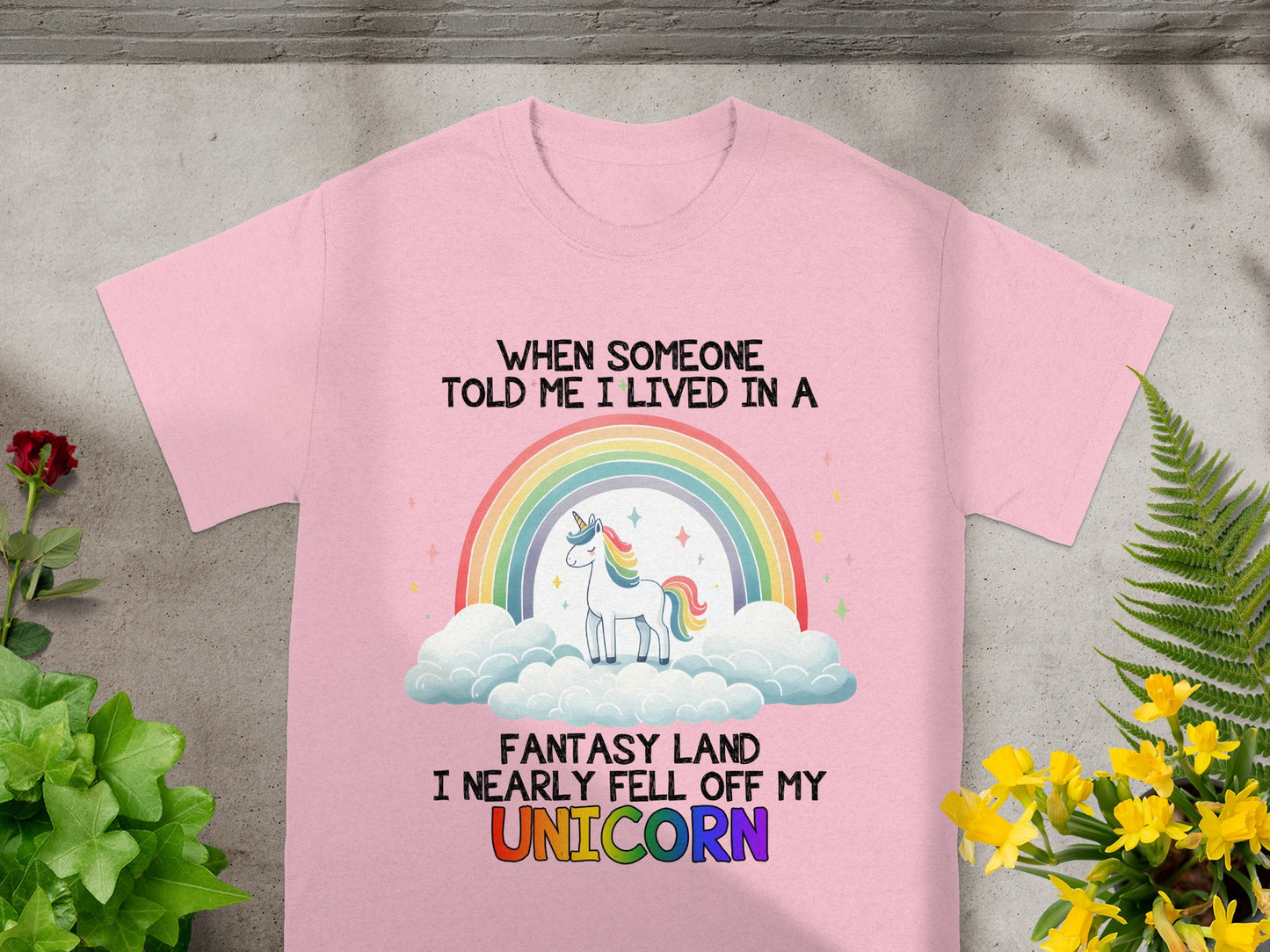 Pink t-shirt with a unicorn, rainbow, clouds, and text "When someone told me I lived in a fantasy land I nearly fell off my unicorn".
