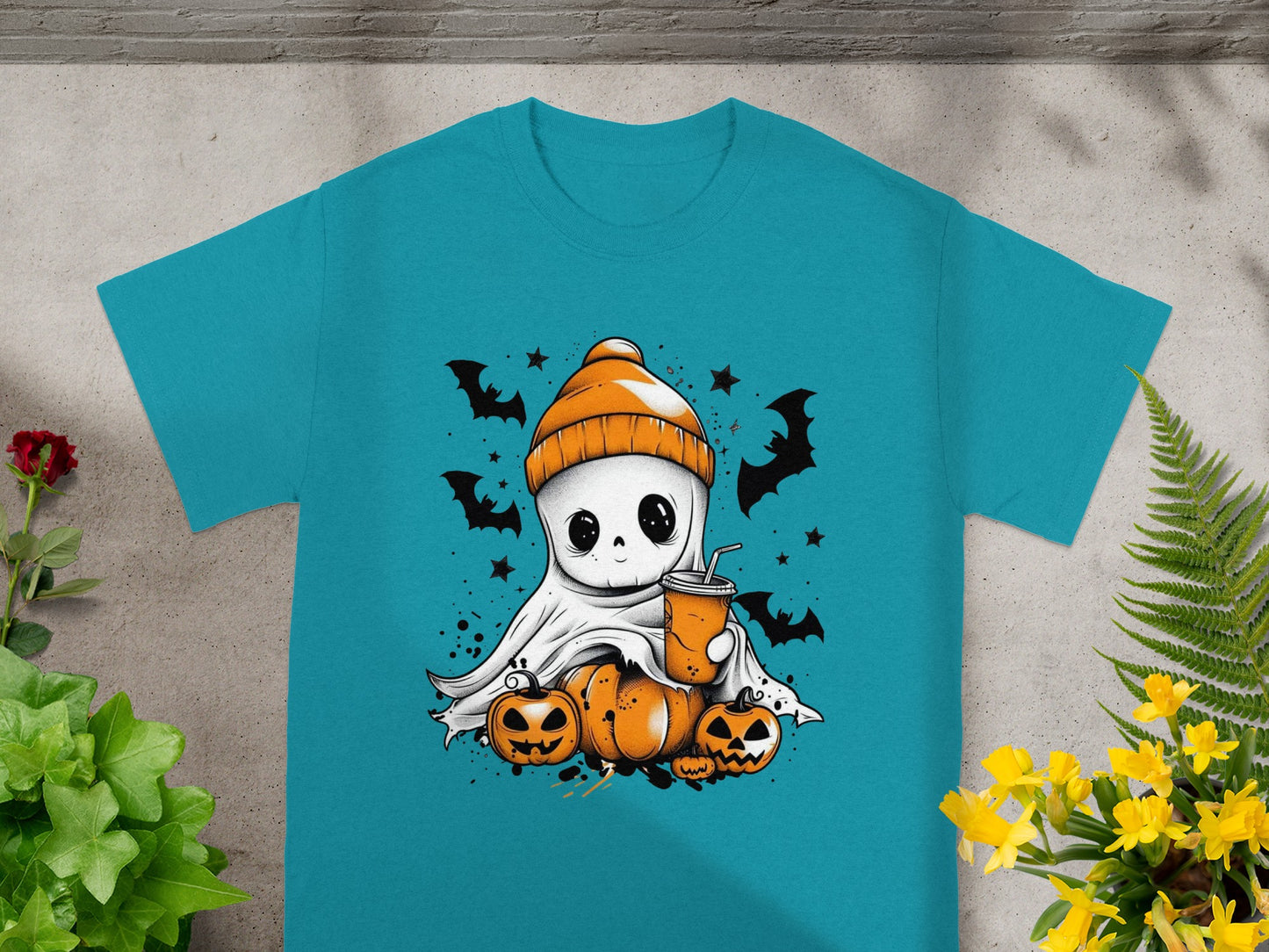 Cute ghost with beanie, pumpkins, and drink surrounded by bats and stars on a teal shirt.