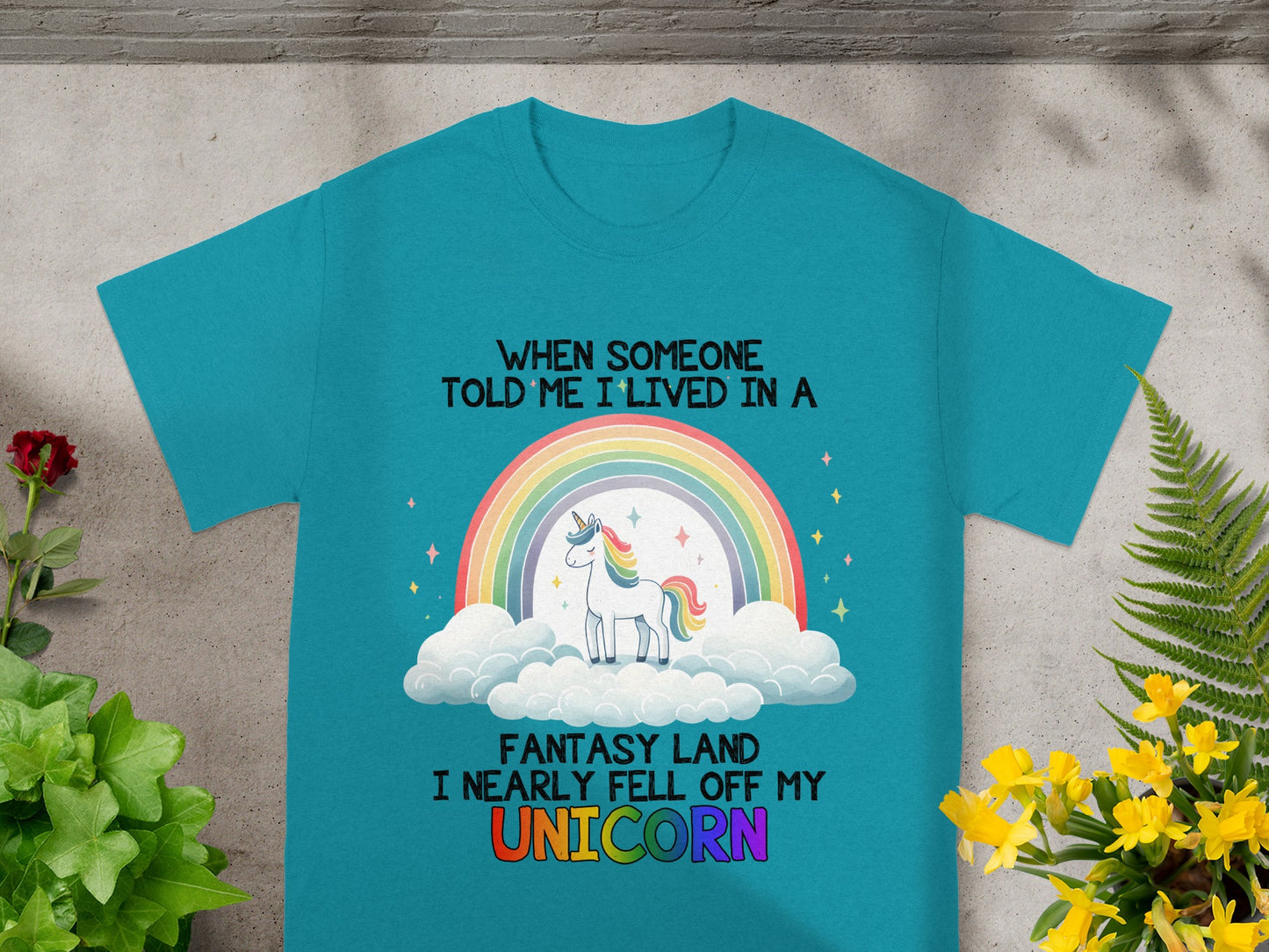 Teal t-shirt with unicorn, rainbow, clouds, and text "When someone told me I lived in a fantasy land I nearly fell off my unicorn."
