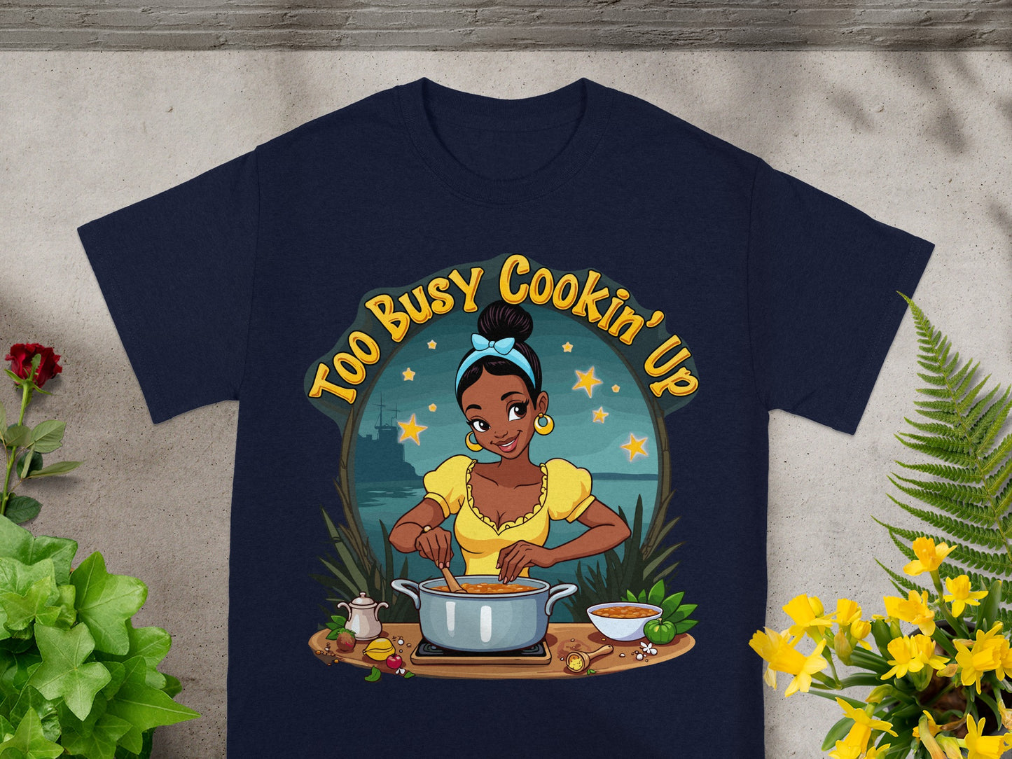 T-shirt graphic with text "Too Busy Cookin' Up" featuring a woman cooking.