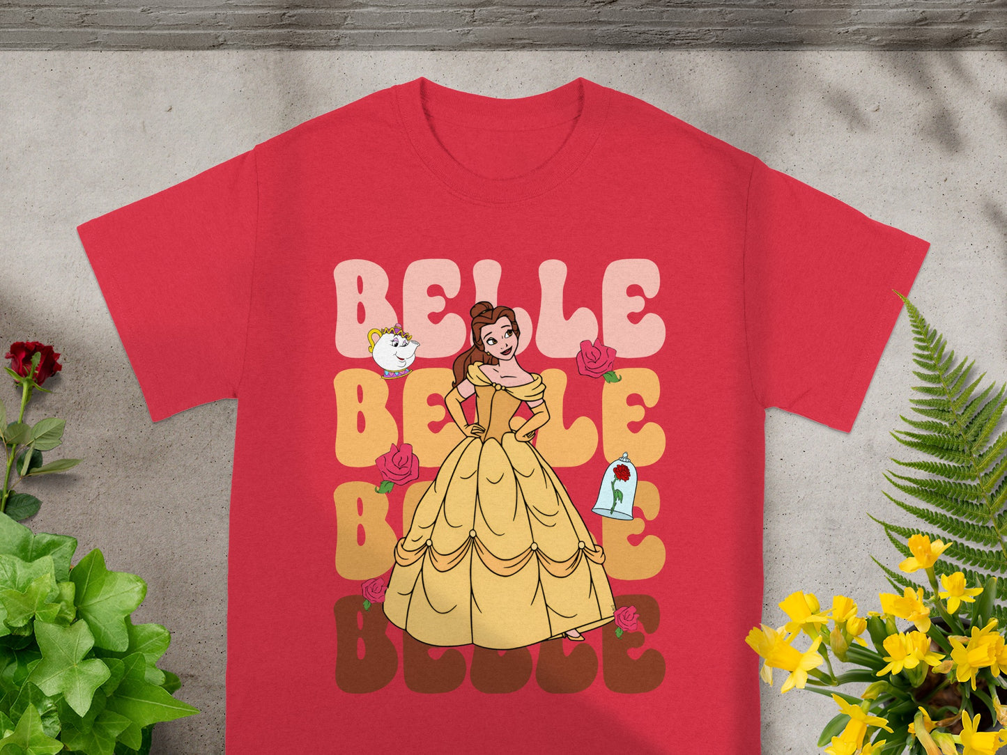 Belle wearing her yellow ball gown, with Lumiere and Cogsworth, against a pink and yellow background.