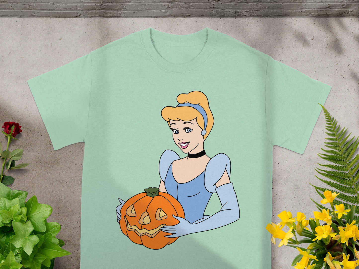 Cinderella holding a carved jack-o'-lantern on a light green t-shirt.