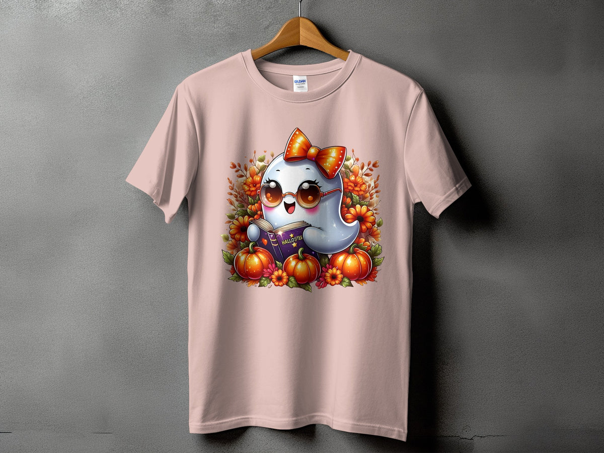 Pink t-shirt with cartoon ghost reading a book surrounded by pumpkins and flowers.