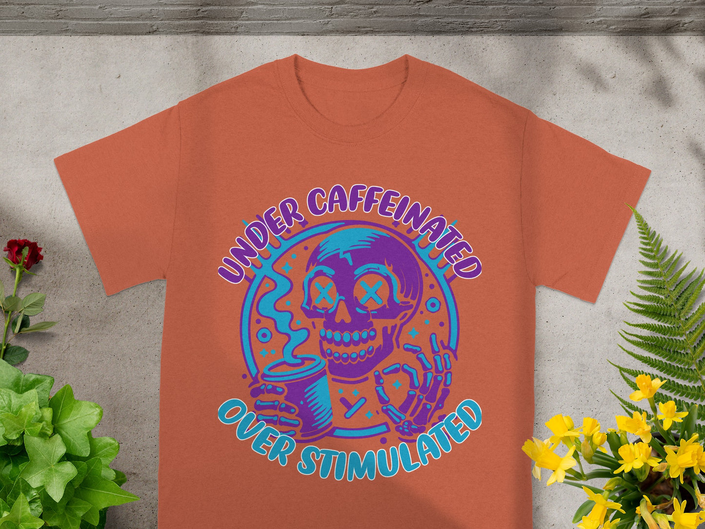 Orange t-shirt with purple and teal "Under Caffeinated Over Stimulated" text on skull graphic.
