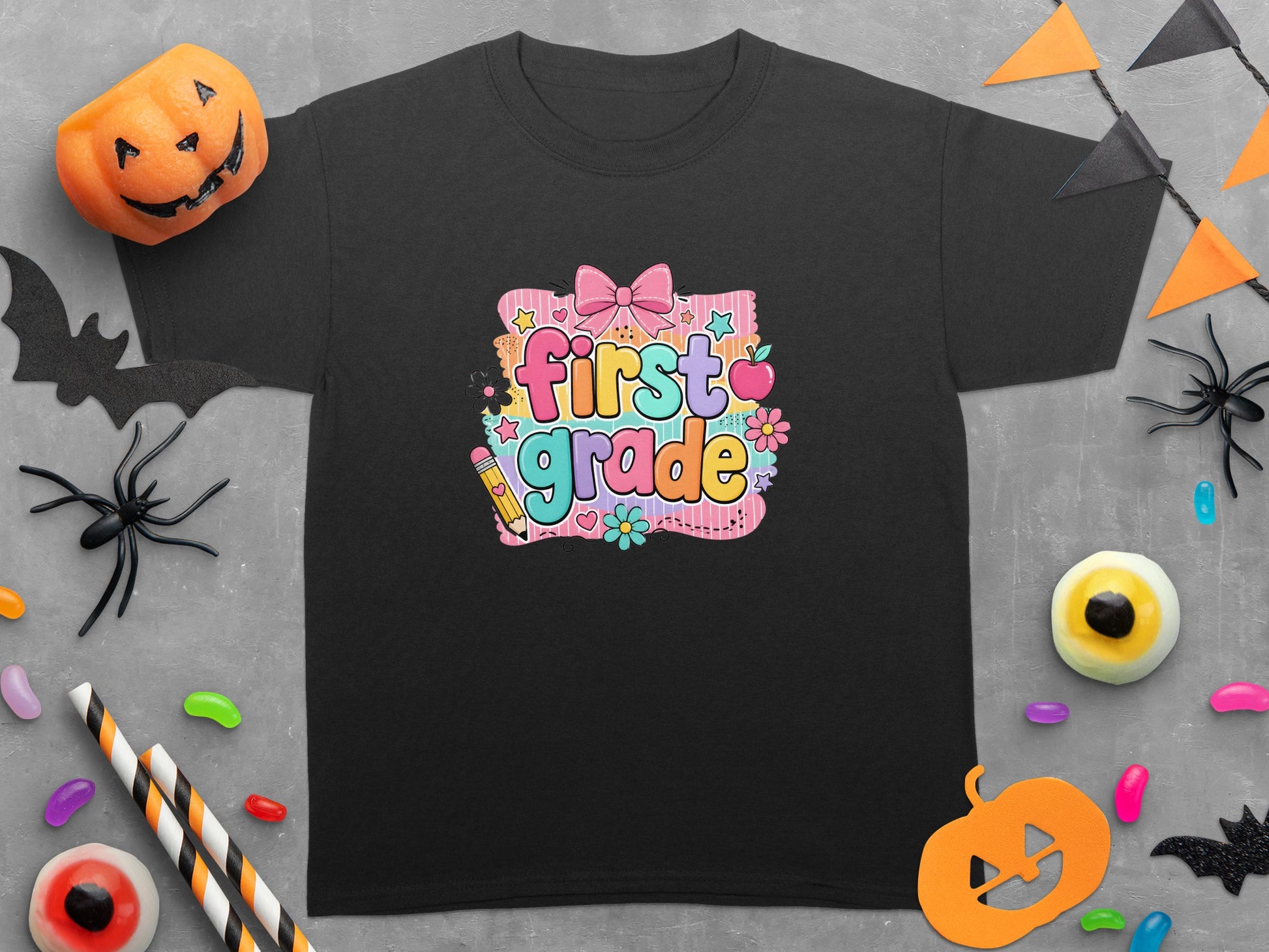 Black t-shirt with colorful "first grade" graphic, surrounded by Halloween decorations and candy.