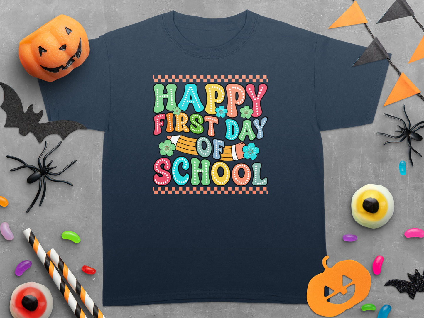 Navy t-shirt with "Happy First Day Of School" in colorful text and Halloween decorations.
