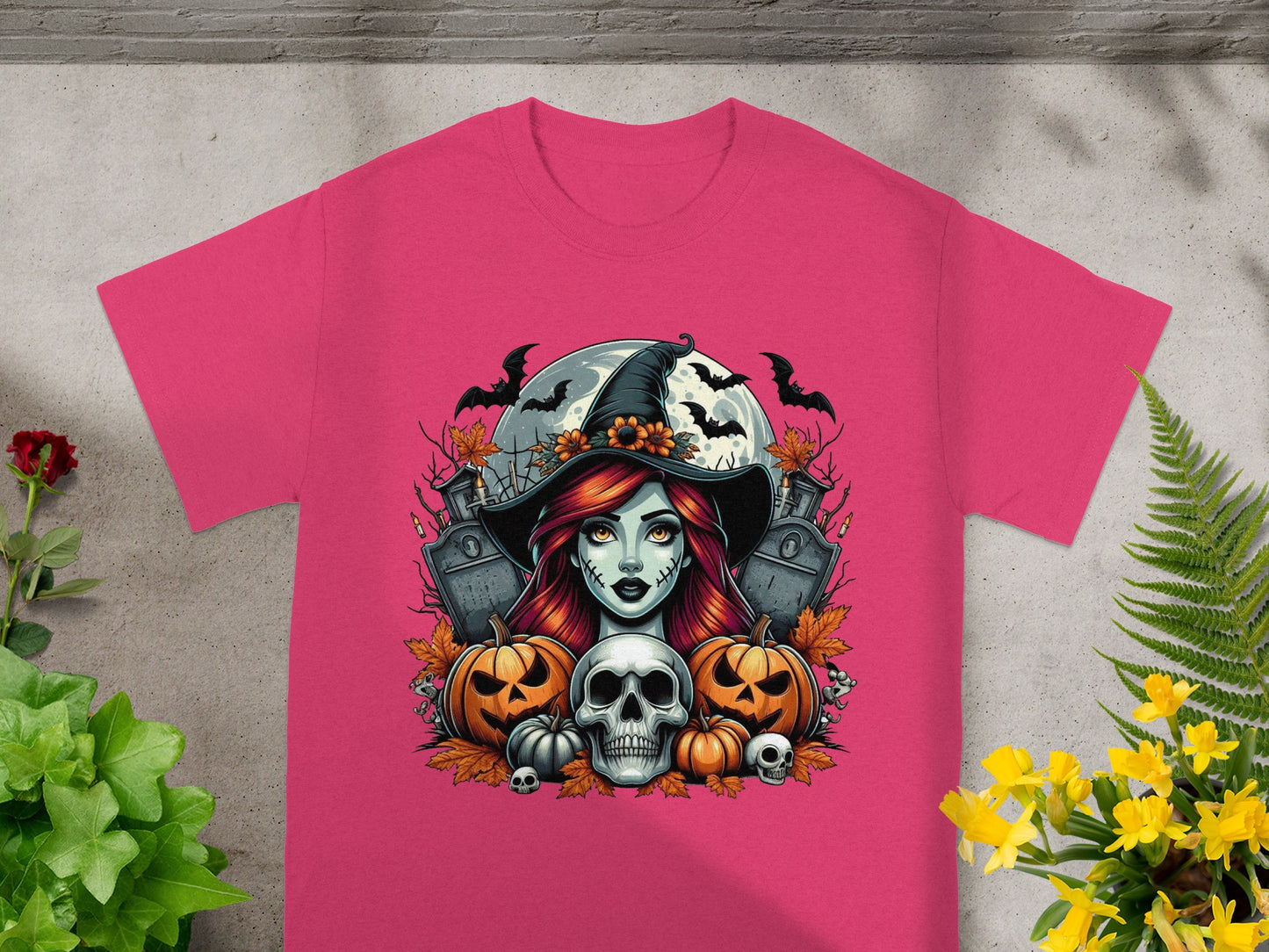 Pink t-shirt with Halloween graphic featuring a witch, pumpkins, skulls, bats, and tombstones.