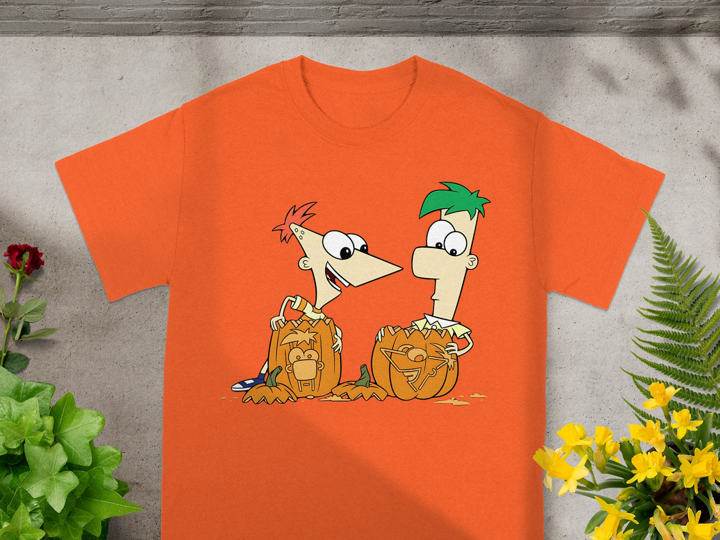 Phineas and Ferb characters carved into Halloween pumpkins on an orange t-shirt.