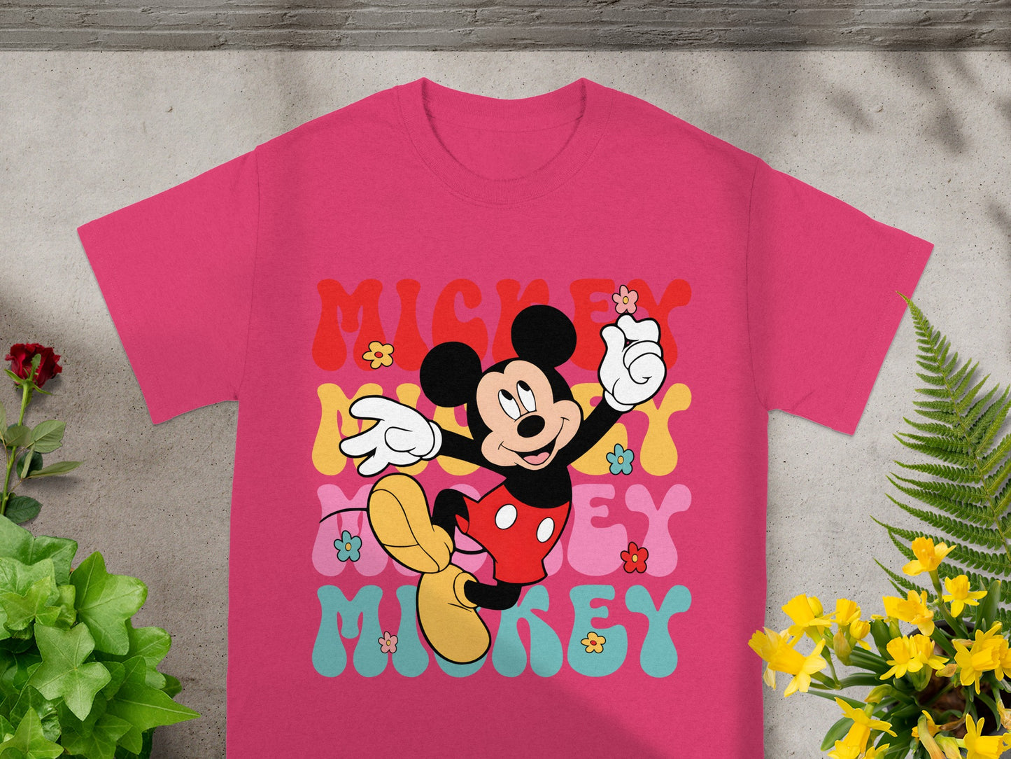 Mickey Mouse graphic on a pink t-shirt with colorful wavy text.