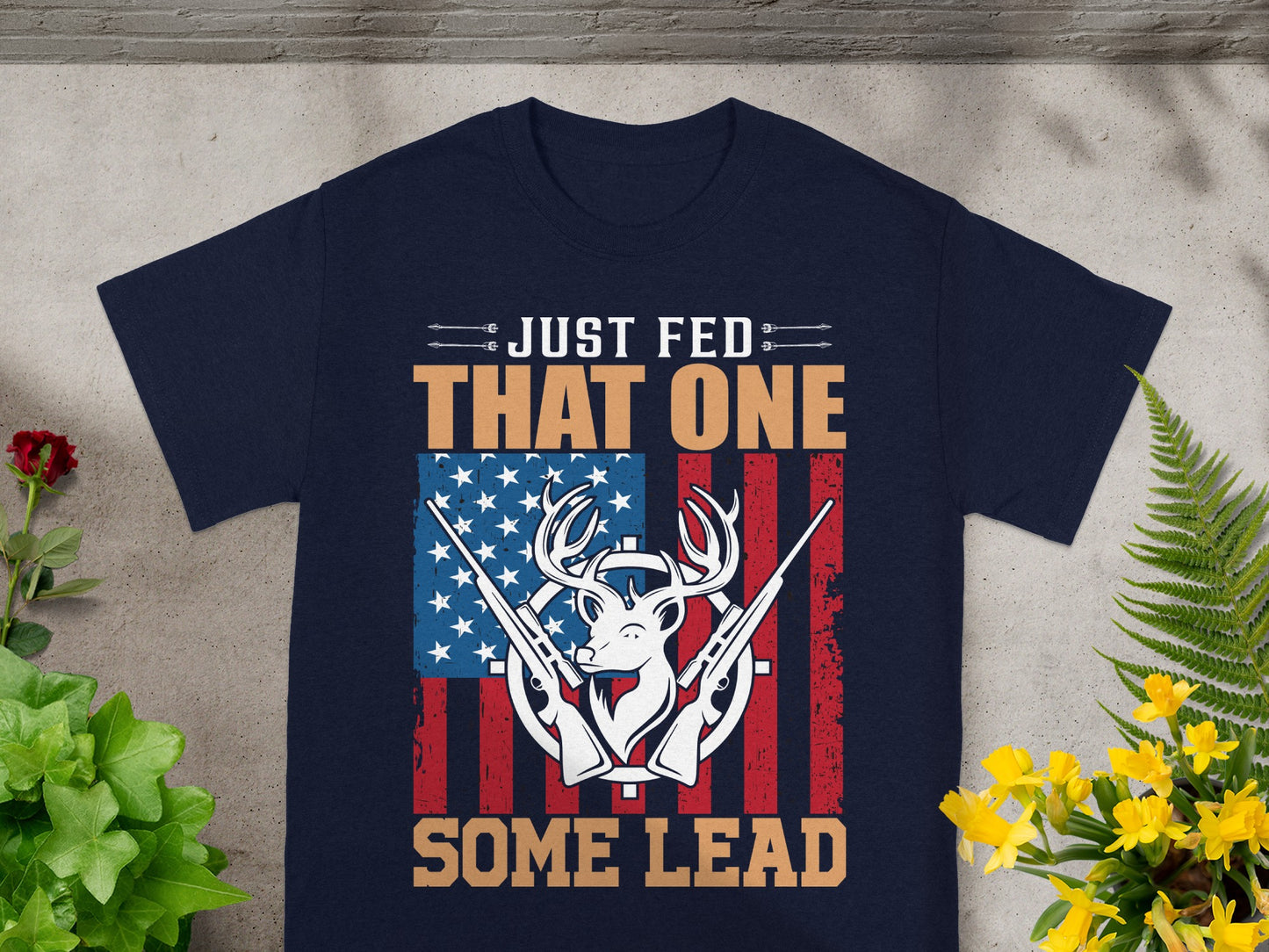 Dark t-shirt with deer, rifles, American flag, and text "JUST FED THAT ONE SOME LEAD".