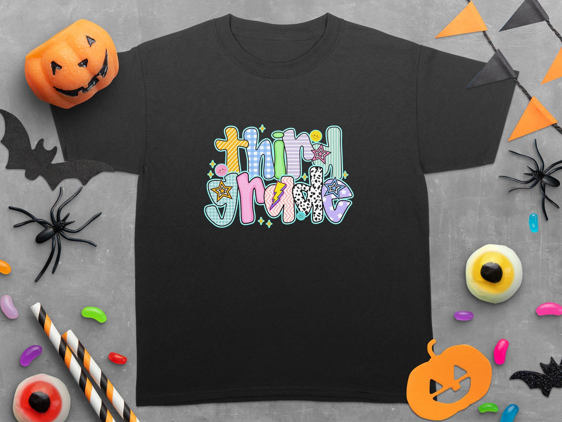 Black t-shirt with colorful "third grade" text graphic and Halloween decorations.