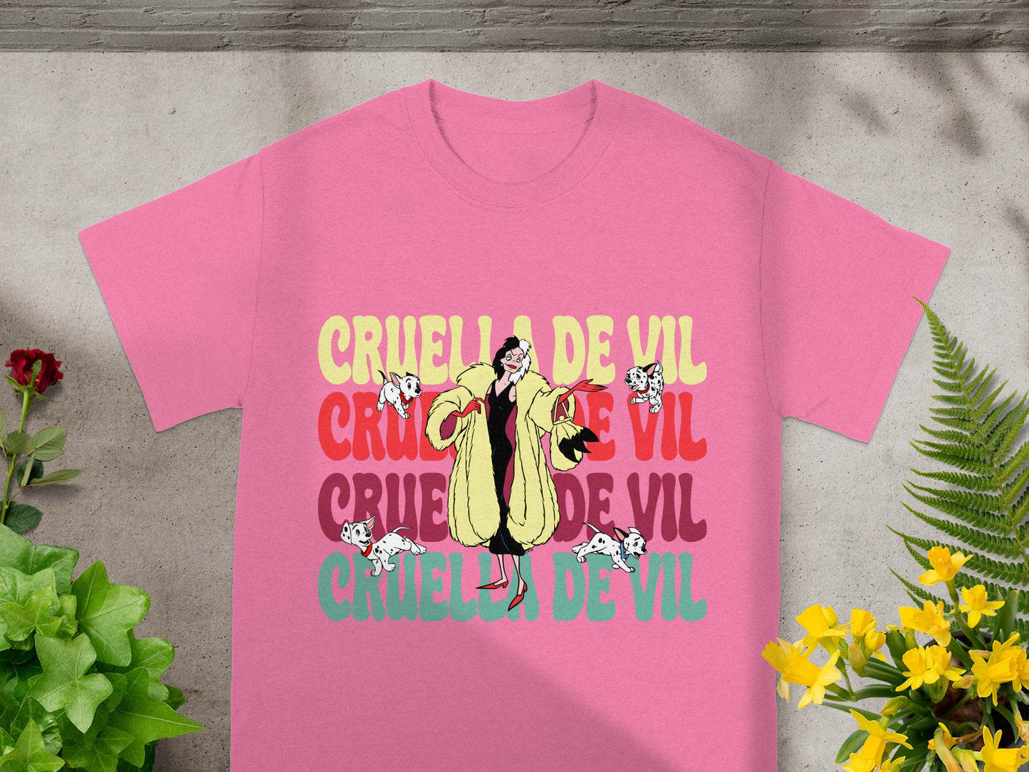 Pink t-shirt with "Cruella De Vil" text and illustrated Dalmatians.