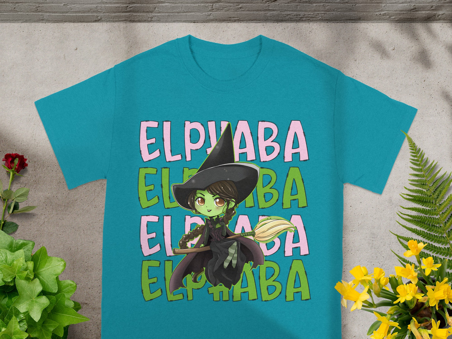 Green witch with broomstick and "ELPYABA" text on teal t-shirt.