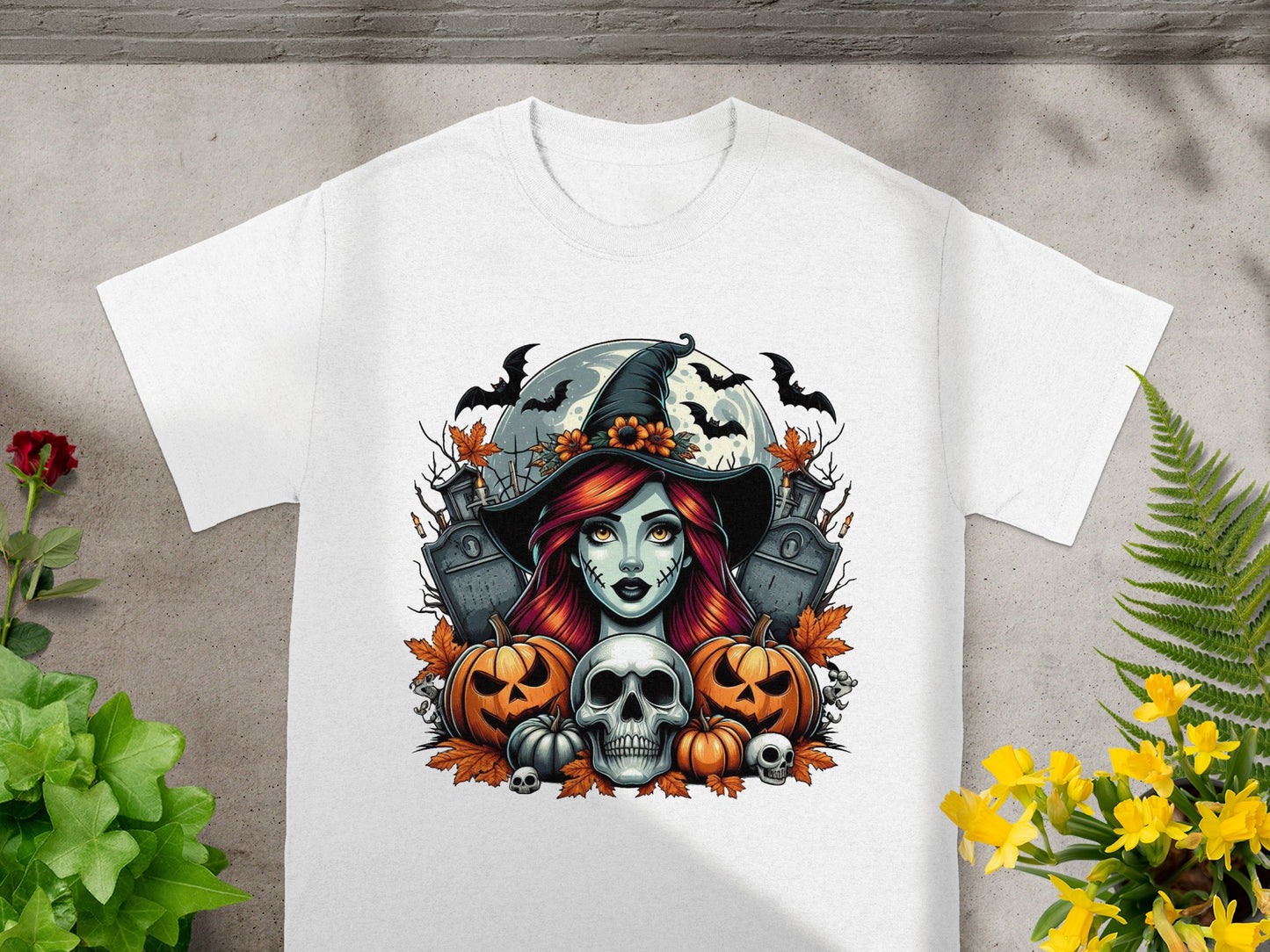Halloween graphic with witch, pumpkins, skull, gravestones, and bats on a white t-shirt.