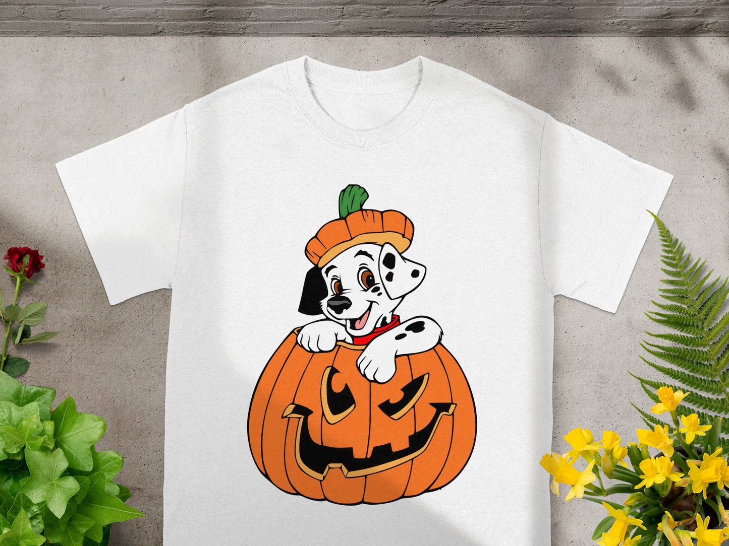 Dalmatian puppy wearing a pumpkin hat peeking out of a jack-o'-lantern on a white t-shirt.