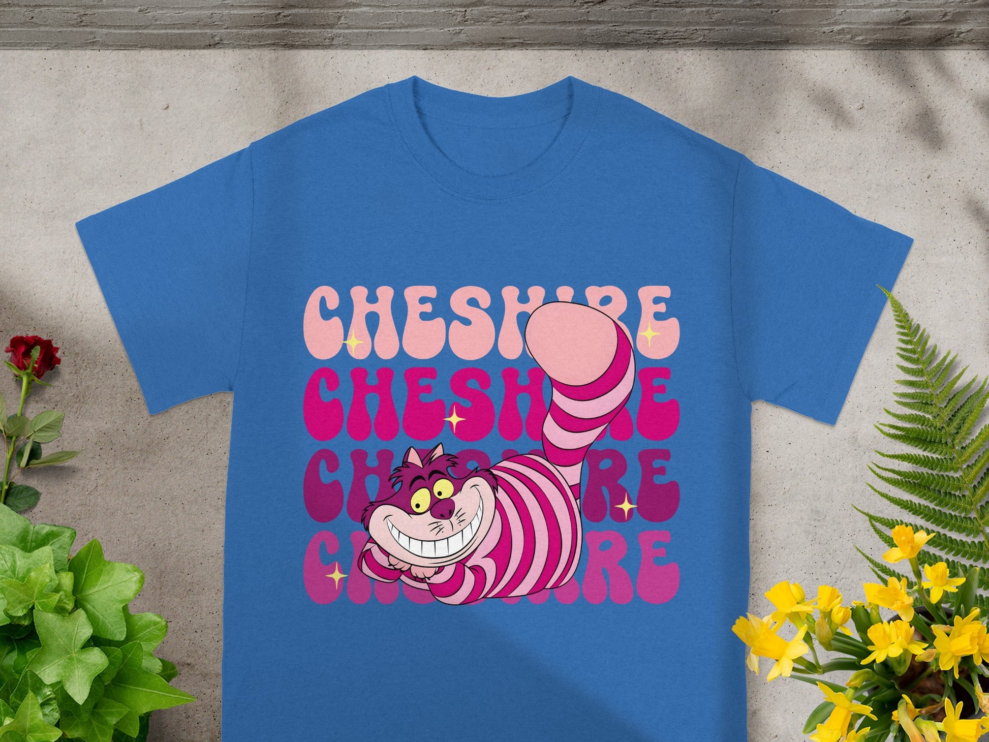 Blue t-shirt with pink and purple Cheshire Cat graphic and text.