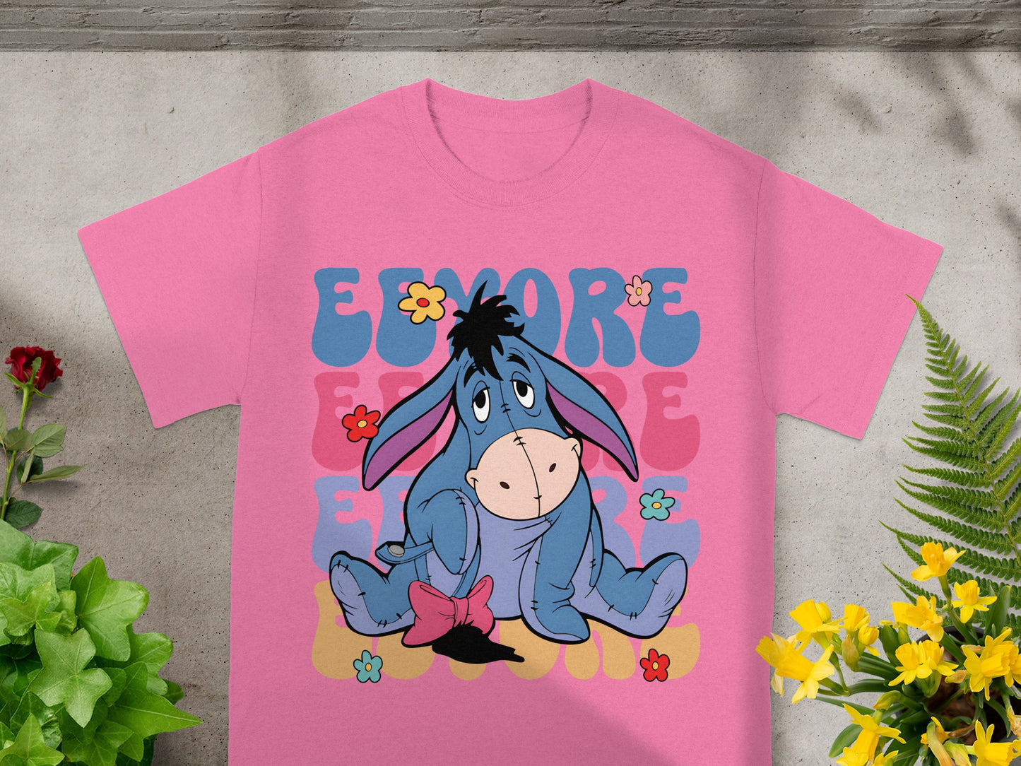 Eeyore sitting on a pink t-shirt with colorful flowers and text.