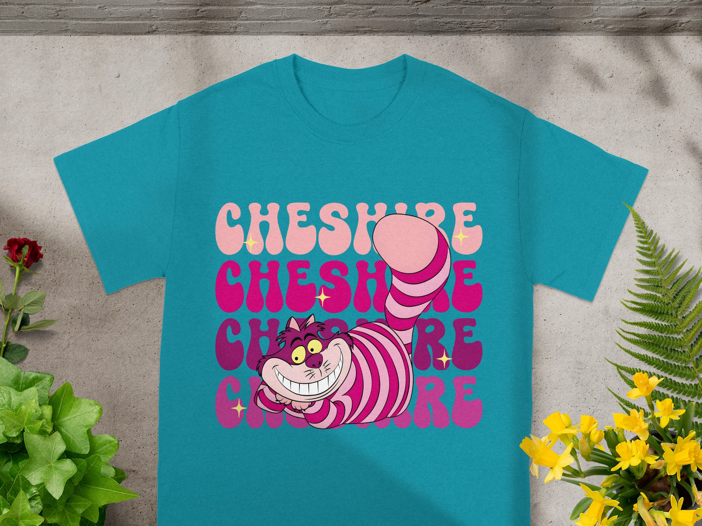 Cheshire Cat graphic on a teal t-shirt with pink text that says "Cheshire Cat."
