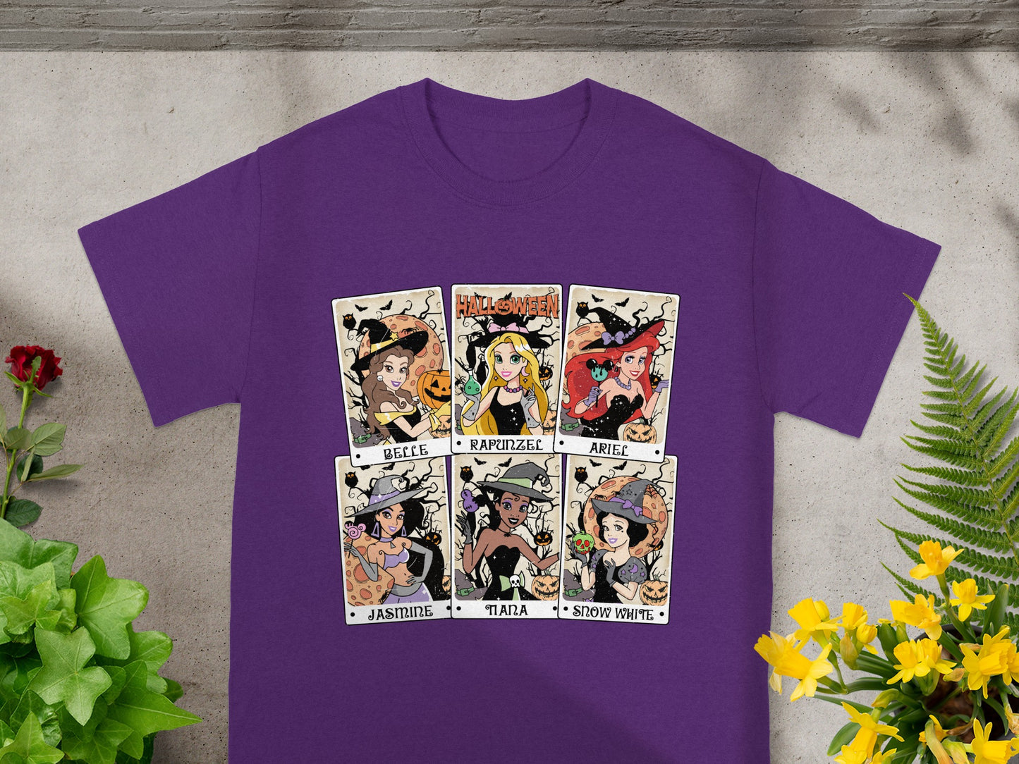Six Disney princesses dressed as witches on a purple t-shirt with Halloween motifs.