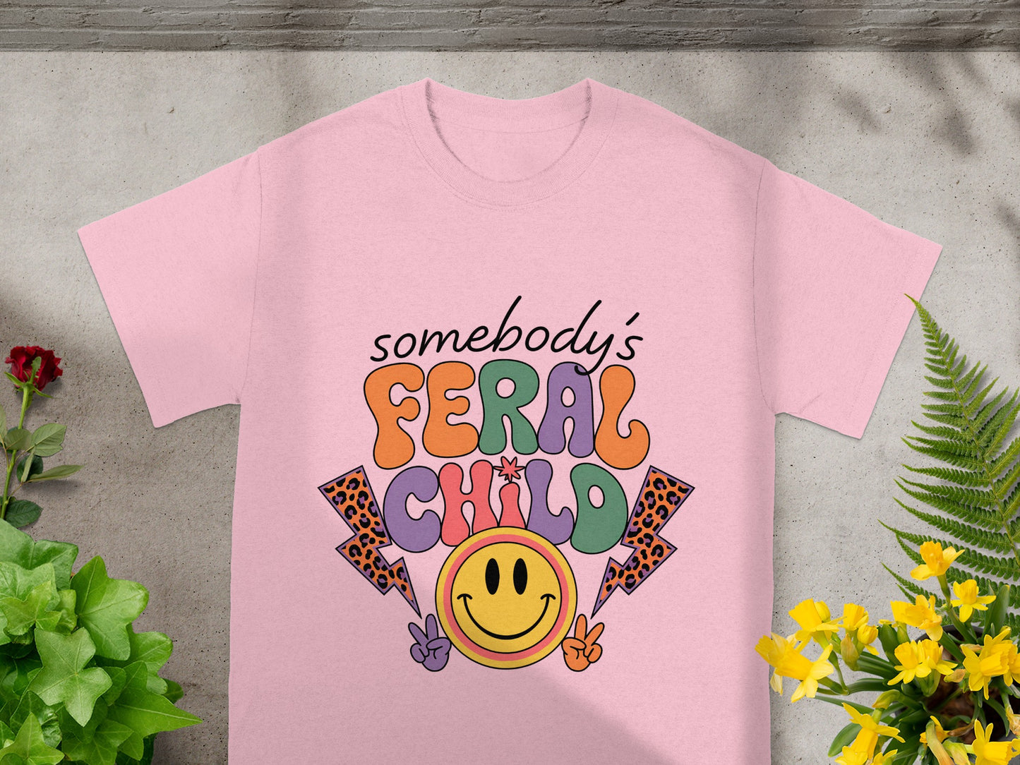 Pink t-shirt with retro "Somebody's Feral Child" text and smiley face design.